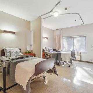 A clean hospital room with a bed and medical equipment by the window.