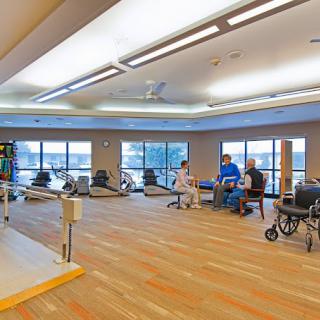 A spacious rehabilitation center with exercise equipment and people engaging in physical therapy.