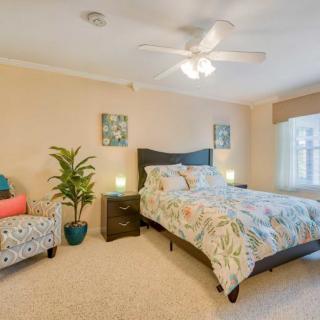 A cozy bedroom featuring a bed with a floral comforter, a chair with colorful cushions, and plants adding a touch of greenery.