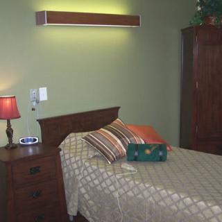 A cozy bedroom featuring a single bed with striped pillows, a wooden nightstand with a red lamp, and a wardrobe.