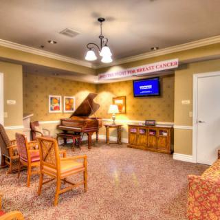 A cozy living room featuring a piano, several chairs, and a television on the wall.