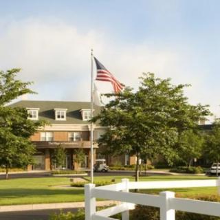 A building with an American flag in front, surrounded by trees and a white fence.