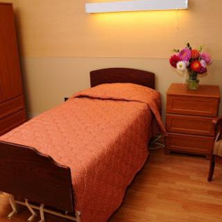 A cozy bedroom featuring a single bed with an orange blanket, a nightstand, and a vase of flowers.