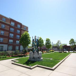 A sunny day in a landscaped park area featuring a statue with a nearby modern building.