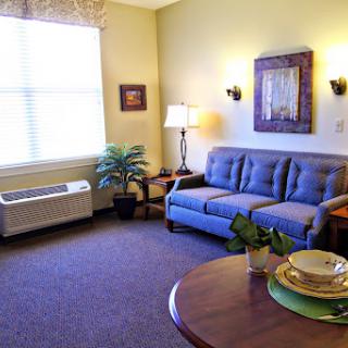A cozy living room featuring a blue sofa, a round table set with plates, and natural light streaming through the window.