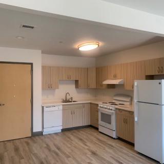 A modern apartment kitchen with light wood cabinets and standard appliances.