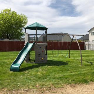 A backyard playground set featuring a slide and swings on a grassy lawn.