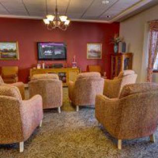 A cozy living room with several armchairs facing a television on a red accent wall.