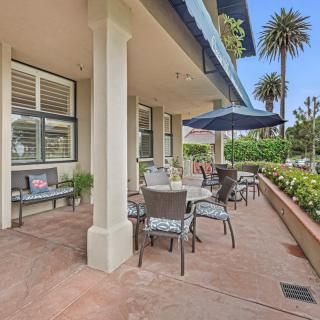 A pleasant outdoor patio with tables and chairs under blue umbrellas, surrounded by palm trees on a sunny day.