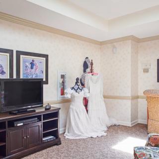 A living room featuring a TV, furniture, and mannequins displaying wedding dresses.