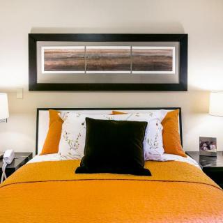 A modern bedroom with orange bedding and stylish artwork above the bed.