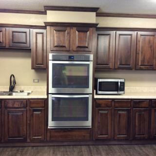 A modern kitchen with wooden cabinets featuring a double oven and microwave.