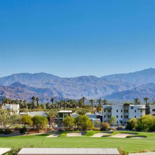 A scenic view of a golf course with mountains in the background and palm trees surrounding modern buildings.