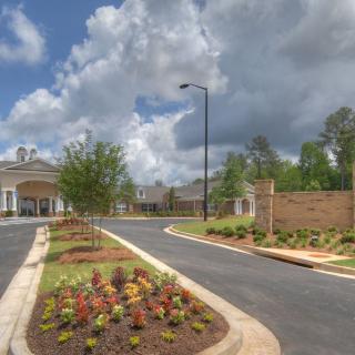 A scenic entrance with landscaped gardens and a paved road under a cloudy sky.
