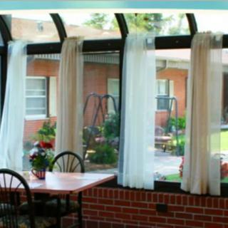 A cozy sunroom with large windows, curtains, and a table with chairs overlooking an outdoor area.