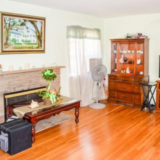 A cozy living room featuring a fireplace, hardwood floors, and a wooden armoire, with a fan and coffee table adding to the decor.