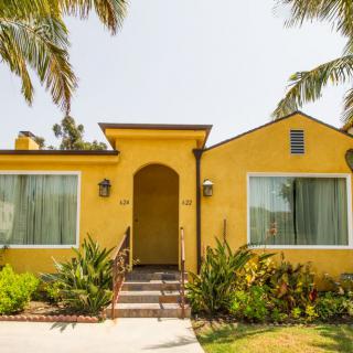 A charming yellow bungalow with a small front yard and palm trees under a clear sky.