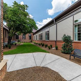 A peaceful courtyard with brick buildings, lush greenery, and a clear blue sky.