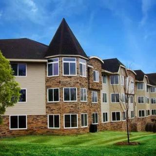 A three-story residential apartment building with a stone and siding exterior, surrounded by well-maintained landscaping under a blue sky.