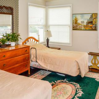 A cozy bedroom with twin beds, a wooden dresser, and a sunlit window.