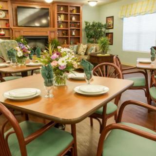 A cozy dining room with tables and chairs arranged neatly, featuring elegant flower centerpieces.