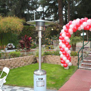An outdoor garden area decorated for an event with a red and white balloon arch and patio heater.