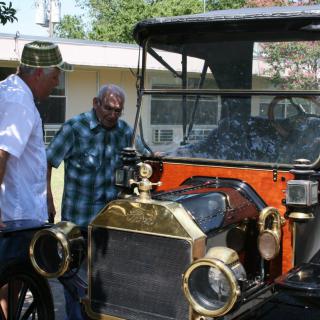 Two individuals admire a vintage car displayed outdoors.