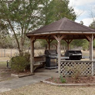 A cozy gazebo in the backyard featuring grills, surrounded by trees and an open field.