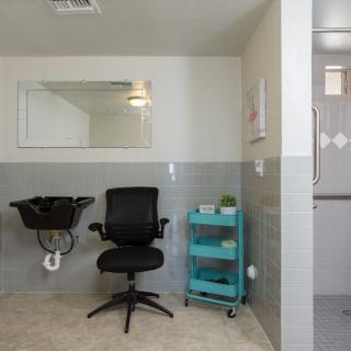 A minimalist salon interior with a chair, sink, mirror, and a turquoise cart.