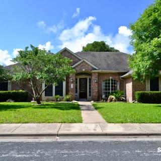 A suburban brick house with a neatly maintained front lawn and trees under a blue sky.