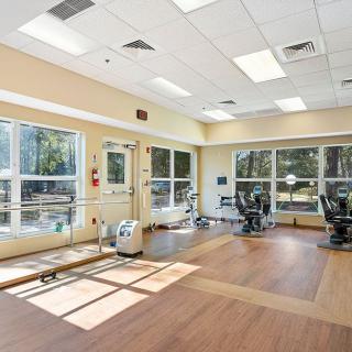 A bright, spacious gym with various exercise equipment and large windows allowing natural light.