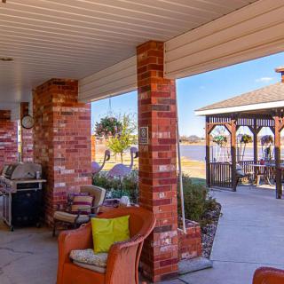 A cozy patio overlooking a lake, featuring brick columns and comfortable seating.