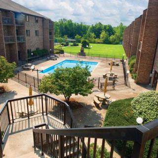 A view of an apartment complex courtyard with a central swimming pool surrounded by greenery and outdoor seating.