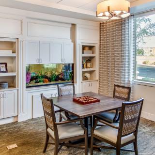 A cozy dining area with a wooden table and chairs, featuring an aquarium and built-in shelves under soft lighting.