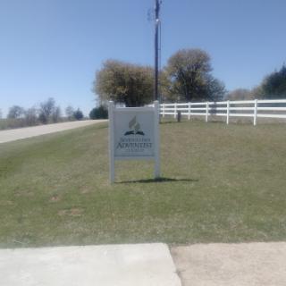 A clear day at a location with a sign, surrounded by green grass and a white fence.