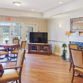 A cozy living area with a television, tables, and chairs arranged on a wooden floor.