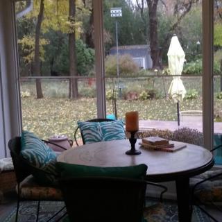 A cozy indoor seating area with a round table and chairs, offering a serene garden view through large windows.