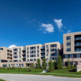 A modern apartment building under a clear blue sky, surrounded by a well-maintained landscape.