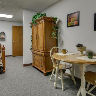 A cozy dining area with a wooden table, chairs, and a cabinet adorned with plants and framed pictures.