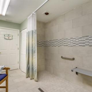 An accessible bathroom with a walk-in shower, handrails, and a shower chair.