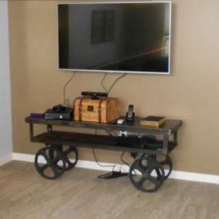 An industrial-style TV stand with large metal wheels, housing electronics beneath a wall-mounted TV.