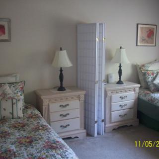 A bedroom with twin beds, floral bedding, lamps, and a room divider.