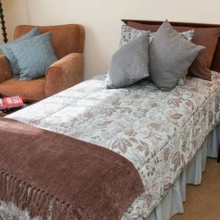 A neatly made bed with several pillows and a blanket in a cozy room with an armchair.