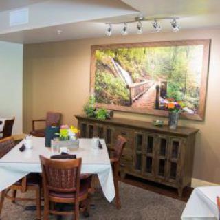 A cozy dining room featuring neatly set tables and a large nature painting on the wall.