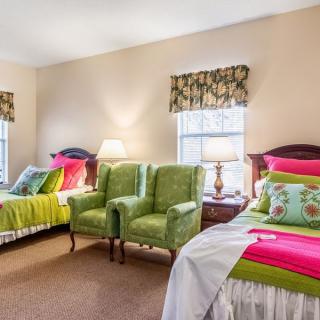 A cozy bedroom with twin beds, vibrant decor, and green chairs by the windows.
