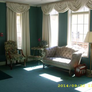 A sunlit living room with a sofa, armchair, and large windows adorned with curtains.