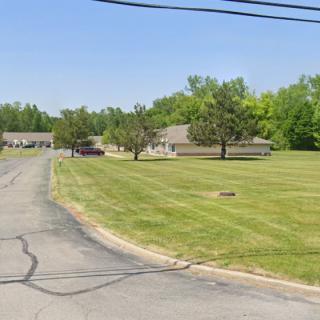 A quiet suburban street lined with houses and well-maintained lawns under a clear blue sky.