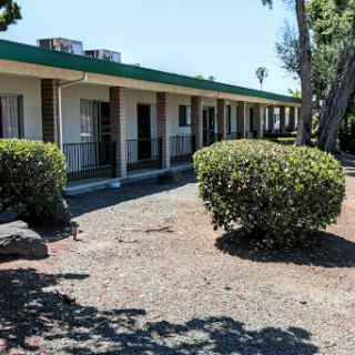 An exterior view of a motel with neatly trimmed bushes under a clear blue sky.