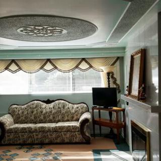 A cozy living room featuring a patterned sofa, decorative ceiling, and a TV stand near the window.