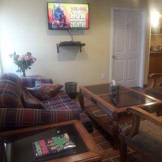 A cozy living room with a sofa, glass coffee table, and a television mounted on the wall.